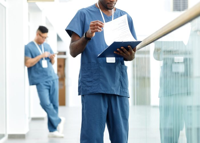 Vertical full length portrait of young African American doctor holding clipboard while standing in hall of modern clinic