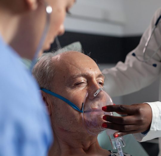Side view of senior patient breathing assisted by respiratory tube Side view of senior patient breathing assisted by respiratory tube in hospital intesive care. African doctor and nurse helping old man to breath sing face mask.